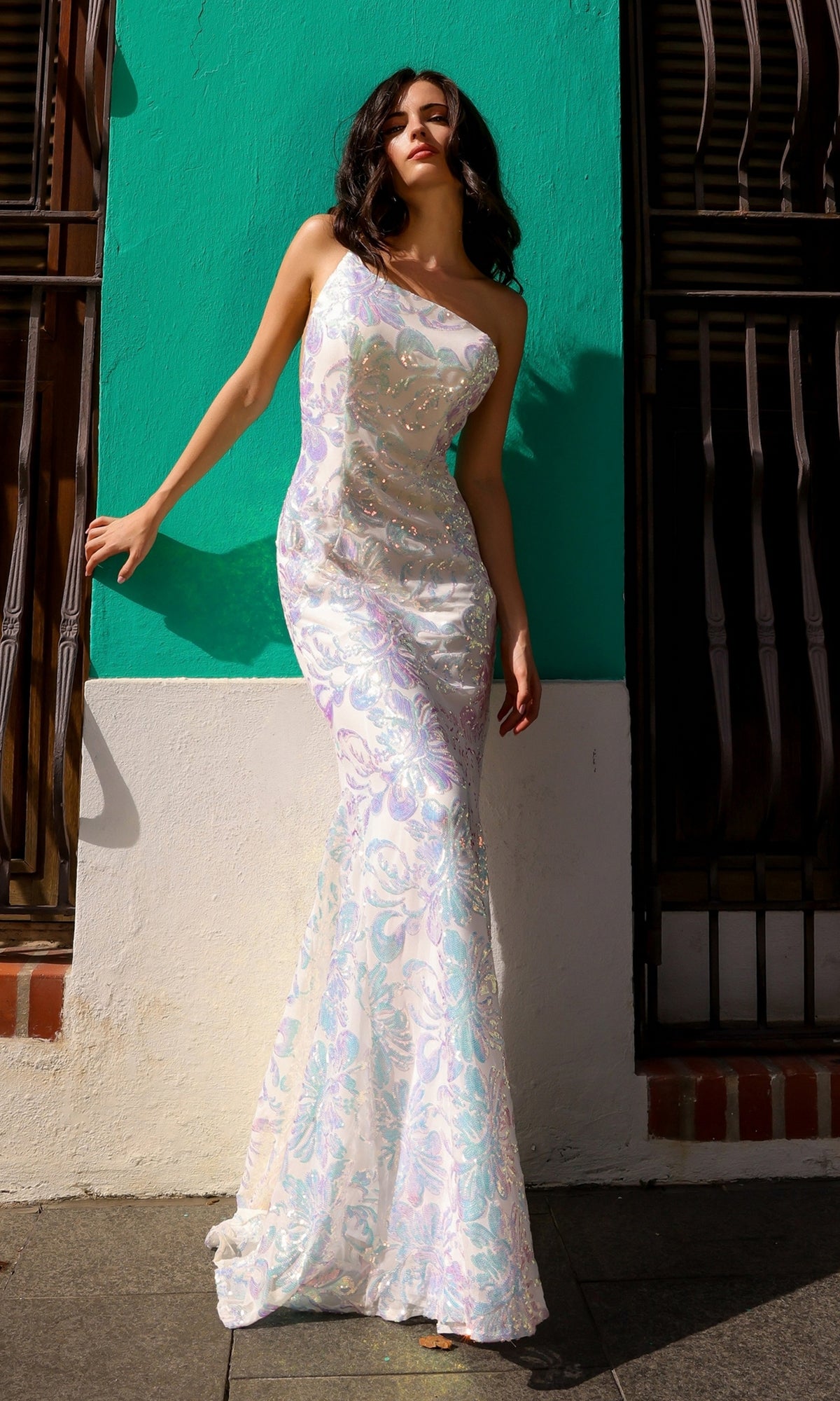 A woman in the One-Shoulder Long Sequin-Print Prom Dress R1308 poses by a turquoise and white wall next to barred windows.